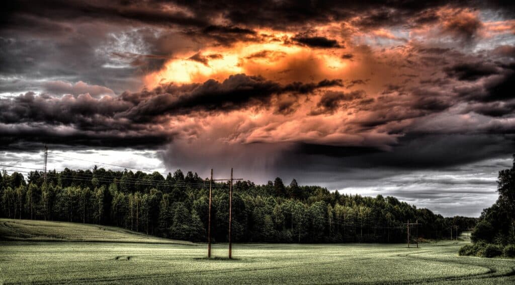 Dramatic storm clouds loom over a green landscape, with dark skies and a glowing orange hue hinting at impending weather changes.